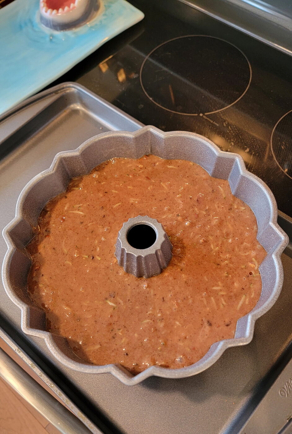 Chocolate-zucchini Bundt dusted with powdered sugar on a glass cake stand, a cut zucchini in front