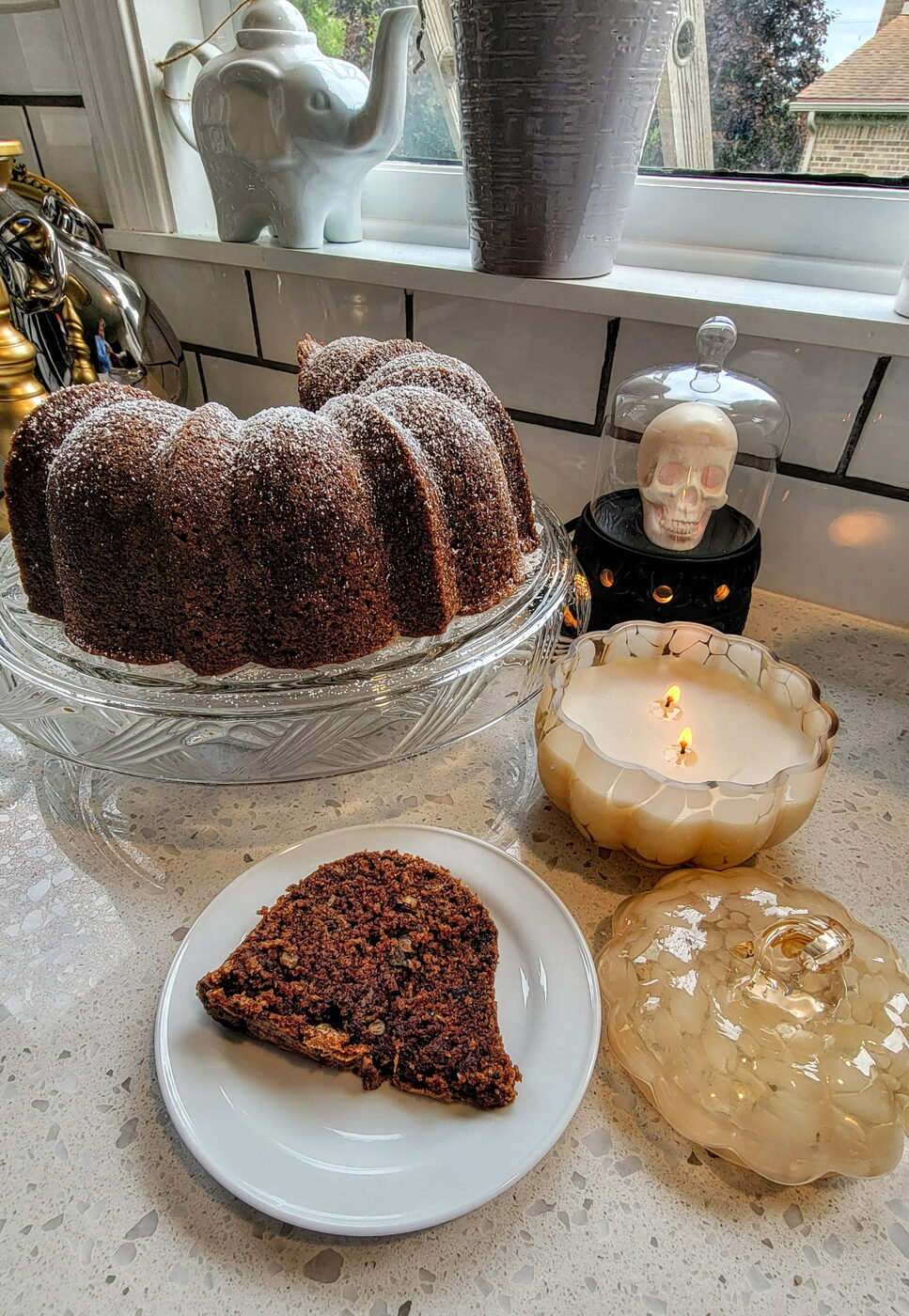 The Bundt with a slice on a plate beside autumn candles